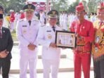 KAPUAS PENGHARGAAN: Bupati Kapuas HM Wiyatno menerima piagam penghargaan sebagai Bupati peduli Radio Tahun 2025 yang diserahkan Kepala Dinas Kominfosantik Kapuas Hartoni U Sawang seusai upacara peringatan HUT ke-80 Kemerdekaan RI di Stadion Olahraga Panunjung Tarung Kuala Kapuas, Minggu (17/8).